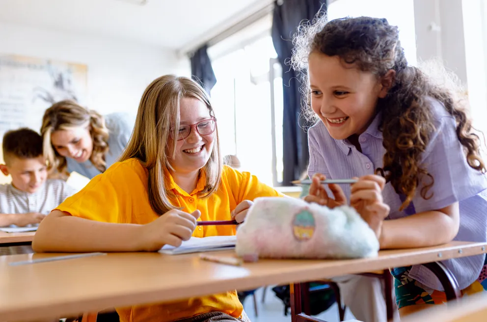Porträt von zwei lachenden und sitzenden Schülerinnen im Klassenzimmer